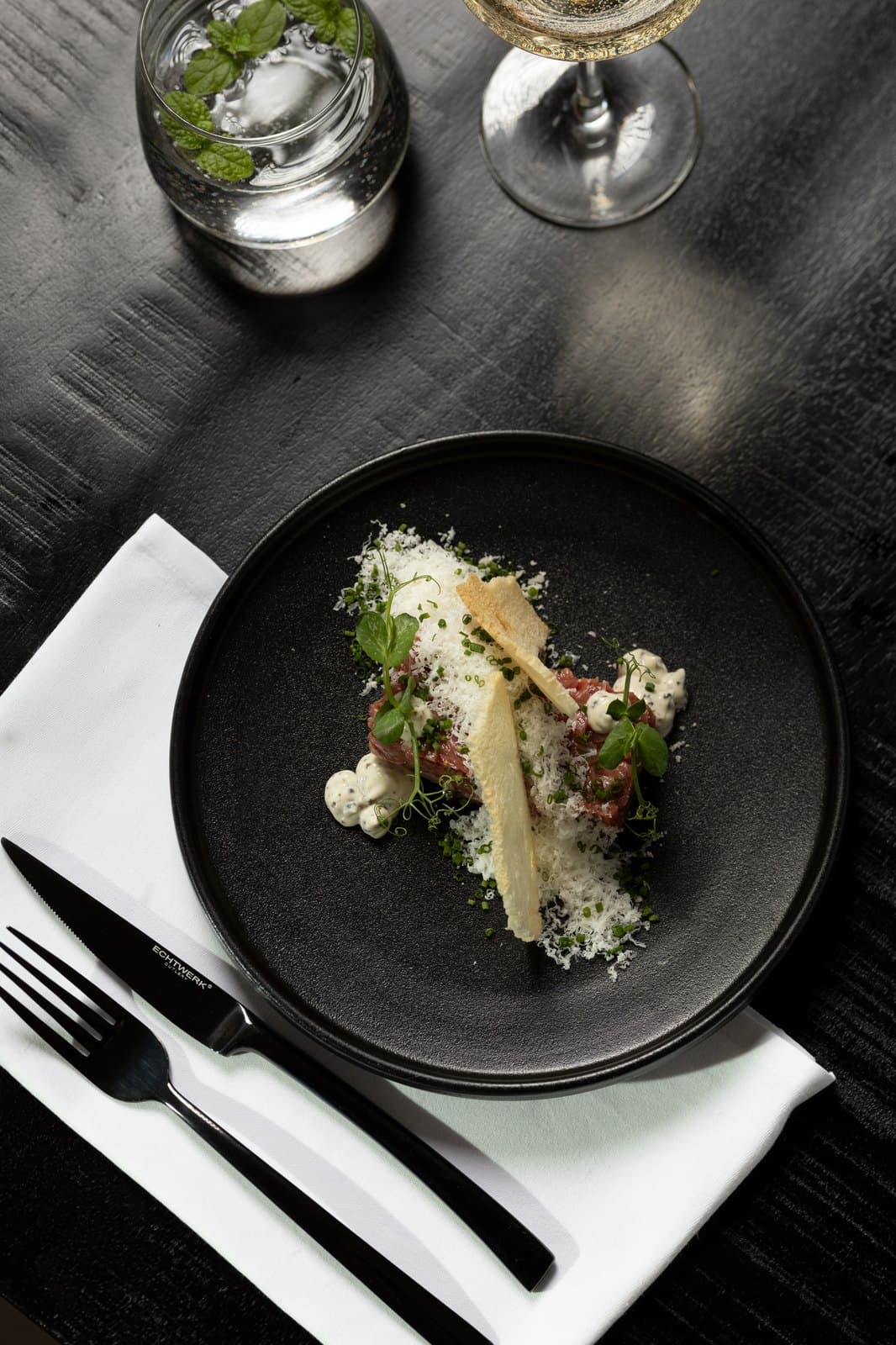 Steak tartaar met geraspte kaas, bieslook en toast op een zwart bord