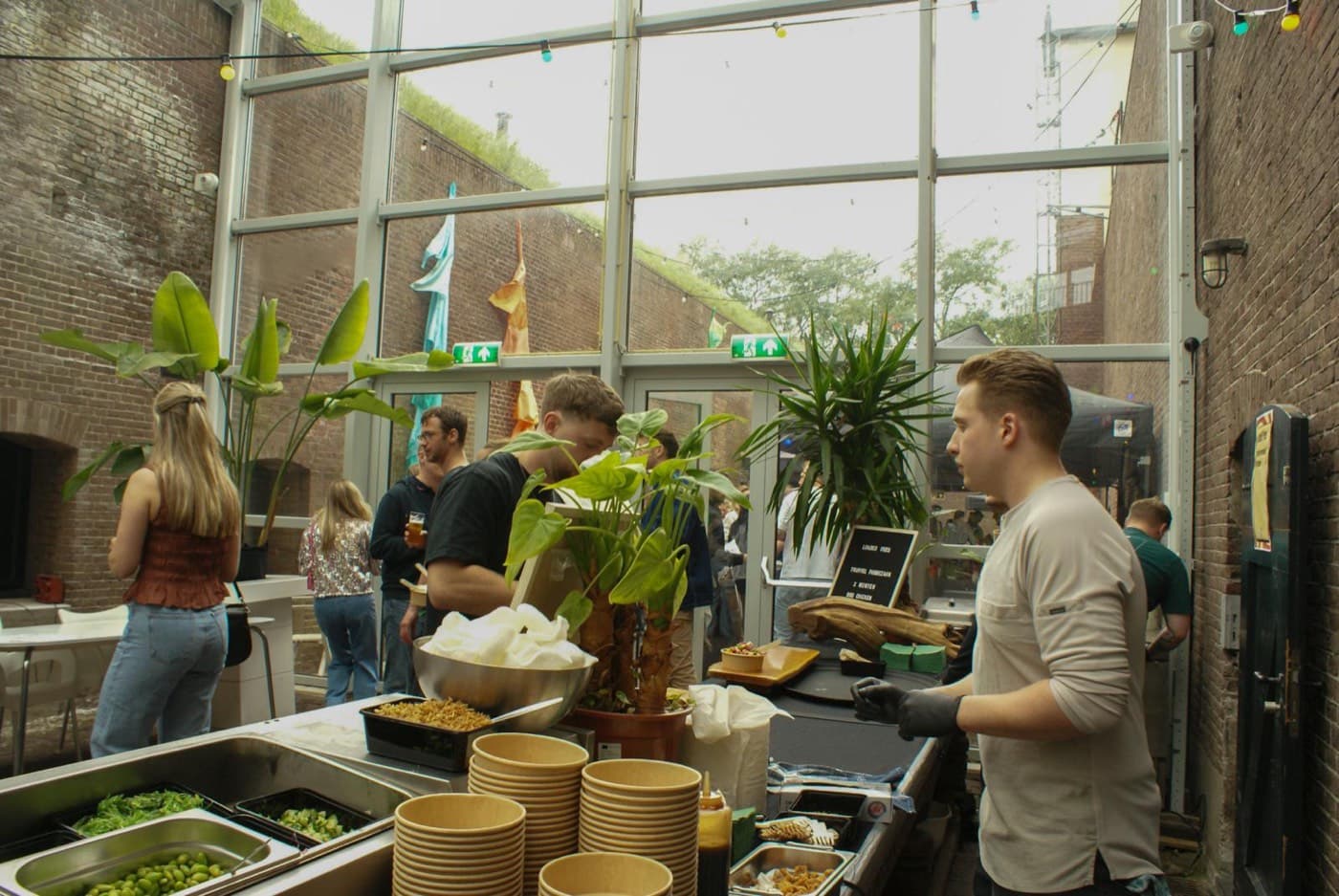 Gasten verzamelen zich rond de live cooking stations in de glazen serre