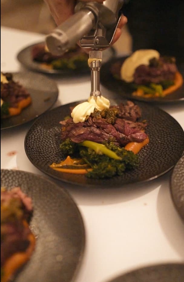 Chef werkt een gang met rundvlees, boerenkool en wortelpuree af aan tafel