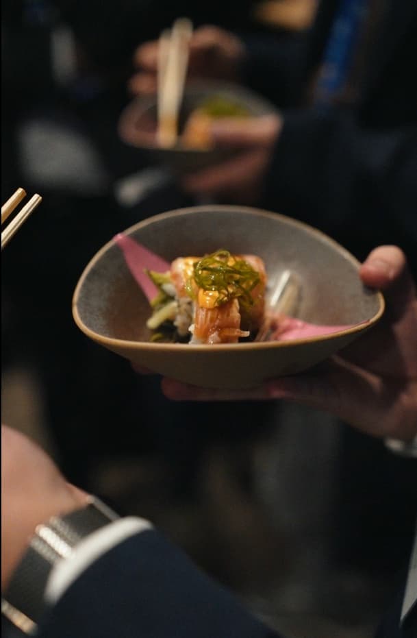 Gast houdt een kommetje vast met sushi van zalm, bosui en spicy mayo